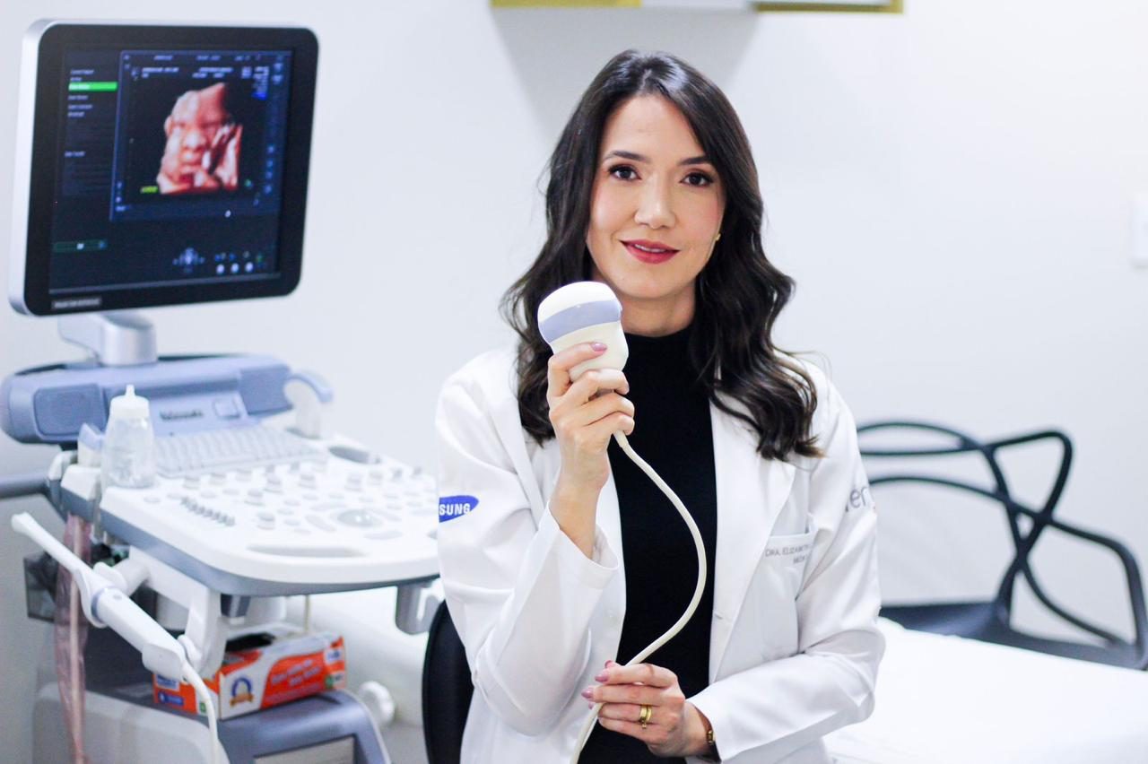 Dra. Elizabeth Curado Sampaio segurando o transdutor de ultrassom ao lado do aparelho